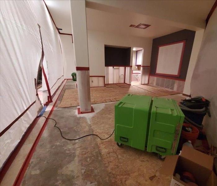 Large room with containment put up and green air movers on the ground.