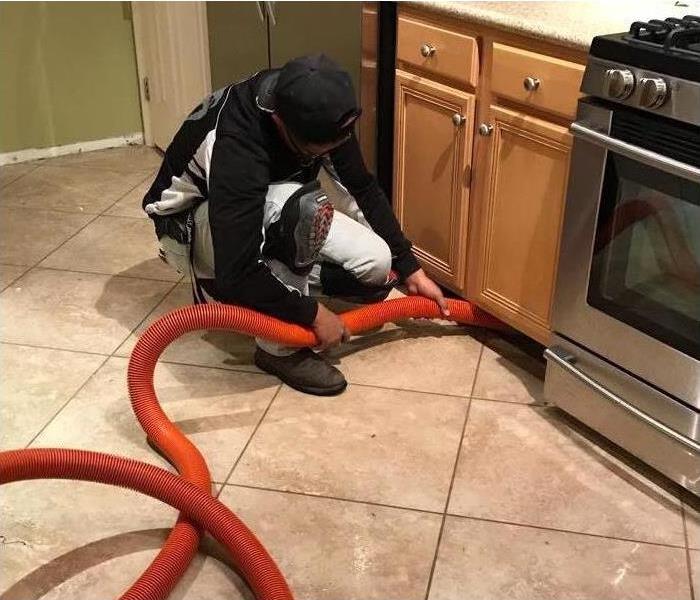 Man holding a red hose under a kitchen sink cabinet due to water damage. Concept of water extraction in a kitchen