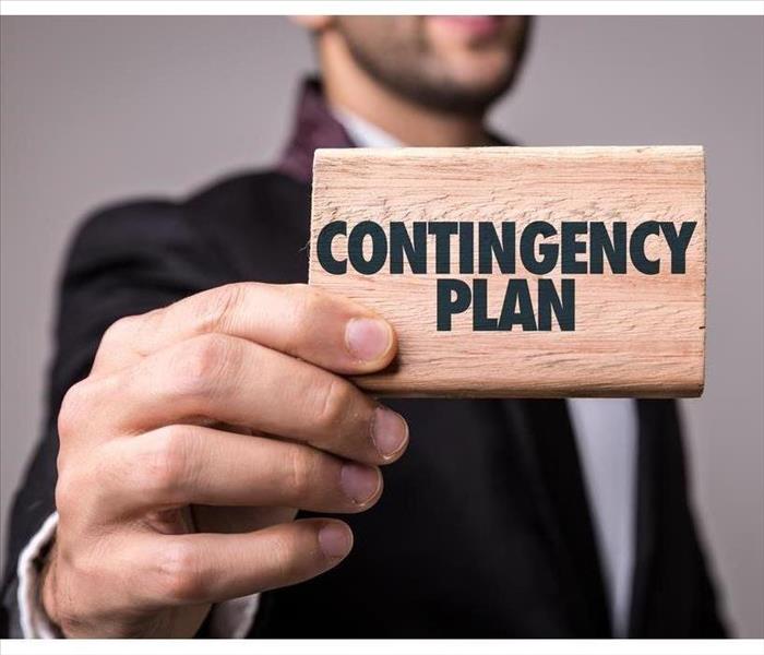 Man holding a piece of wood that says Contingency Plan